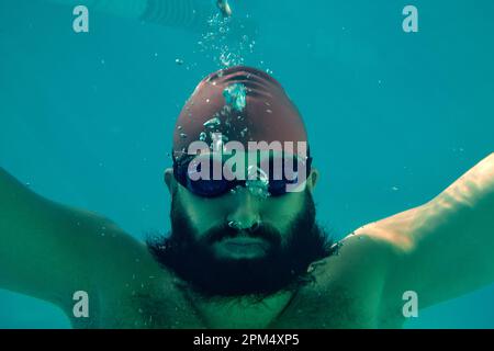 Professional male swimmer practising in swimming pool. Underwater shot of young sportsman swimming in pool. Stock Photo