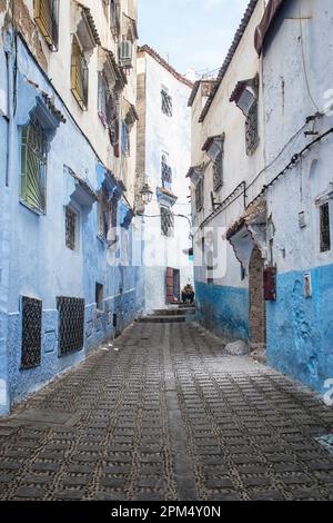 A man sitting in one of the many narrow streets of the blue city of Chefchouen, Morocco. Stock Photo