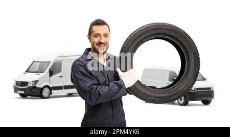 Auto mechanic holding a tire in front of two white vans isolated on white background Stock Photo