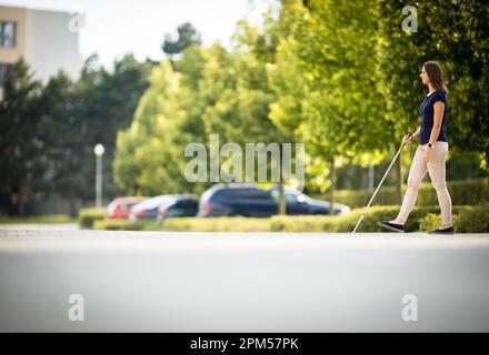 Young woman with vision impairment walking on city streets, using her white cane Stock Photo