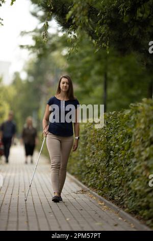 Young woman with vision impairment walking on city streets, using her white cane Stock Photo