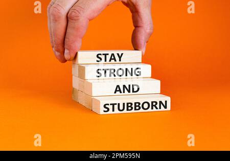 Stay strong and stubborn symbol. Concept words Stay strong and stubborn on wooden block. Beautiful orange table orange background. Motivational busine Stock Photo