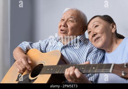 Senior man playing acoustic guitar and singing with his wife at home Stock Photo