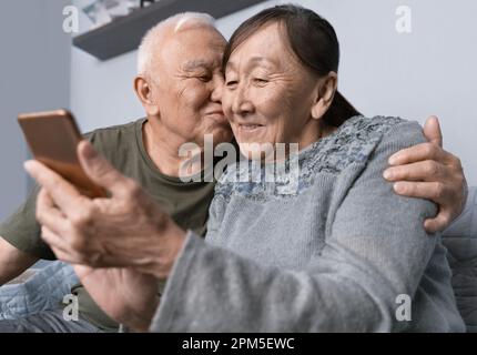Senior couple using smartphone. Senior man kissing his wife Stock Photo