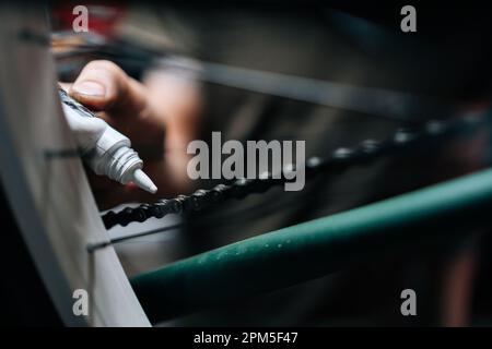 Detail cropped shot of unrecognizable man greasing, oiling, lubricating links of bicycle chain, entering inside each link in dark garage. Stock Photo