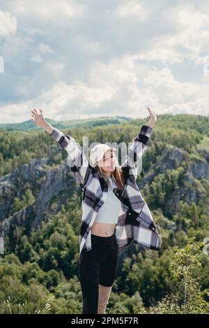 a girl in a checkered shirt raised her hands high in the mountains Stock Photo