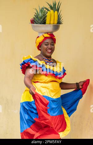 Happy smiling Palenquera fresh fruit street vendor dancing in Cartagena de Indias, Colombia. Cheerful Afro-Colombian woman in traditional costumes. Stock Photo