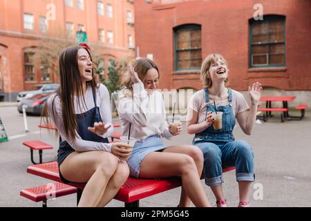 Women friends laughing while sitting on table in outdoor courtyard Stock Photo