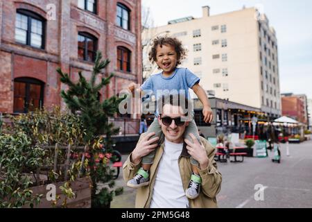 Man walking downtown with happy toddler son on his shoulders Stock Photo