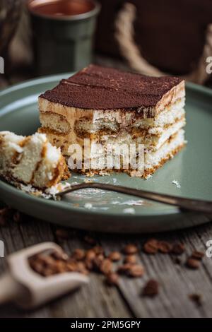 A piece of Tiramisu cake, traditional Italian dessert, served in moody, rustic scene. Wooden background and green plate. Stock Photo