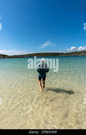 Woman walking in clear turquoise water at Dog's Bay Stock Photo