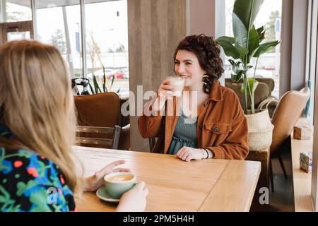 Two happy women meeting up for coffee inside Stock Photo