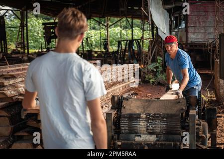 Adult man working on woodworking machines in carpentry shop with his son. Family business. Stock Photo