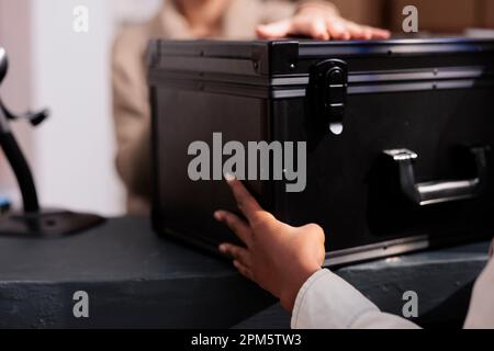 Retail store stockroom employee giving colleague black case at reception desk. Warehouse operator making customer order registration and checking product in stock at counter close up Stock Photo
