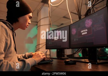 Young man being confused about critical error warning message on screen, trying to hack database program. Professional cybercriminal using malware to crack firewall encryption, data breach. Stock Photo