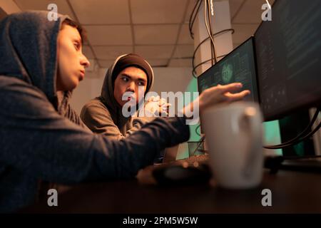 Hackers planning cyberattack, discussing malicious software code, criminals breaking into database, stealing information. Internet fraud, scammers hacking computer system at night time Stock Photo