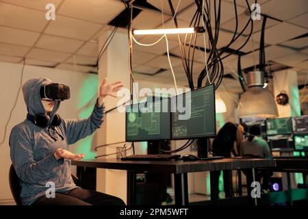 Cybercriminal working with professional vr glasses to crack encryption, trying to steal personal information and passwords. Female thief planting malware on virtual reality 3d headset. Stock Photo