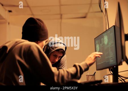 Cyberattack, criminals hacking database, stealing electronic information. Cybercrime, data breach, man and woman hackers in hoods breaking into online server, coding malicious software Stock Photo