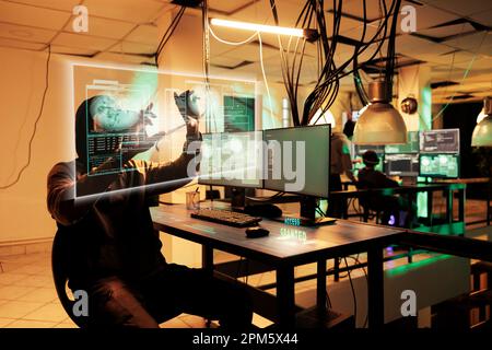 African american hacker breaching database with holograms and AI, using futuristis display in fron of him, wearing virtual reality headset Stock Photo