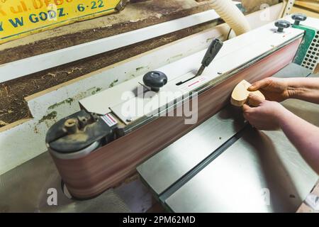 Unrecognizable carpenter working on a wooden piece using professional grinding machine. Wood goods creation process. High quality photo Stock Photo