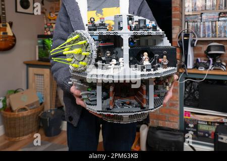 A man in his thirties holding a Lego model of the Star Wars Imperial Death Star at home, UK. A retired product. Theme: adult hobbies, Lego fan Stock Photo