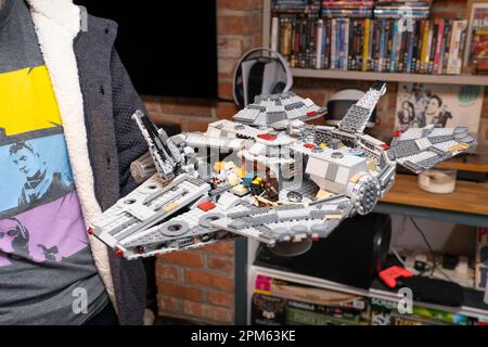 A man in his thirties holding a Lego model of the Star Wars Millenium Falcon at home, UK. A retired product. Theme: adult hobbies, Lego fan Stock Photo