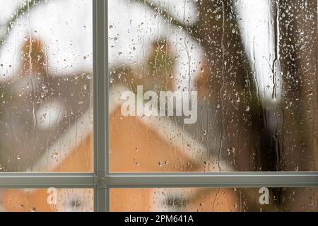 Rain hitting a running down a house window in March, England. Theme: saving for a rain day, rainy day fund, spring weather, rainy days, staycation Stock Photo