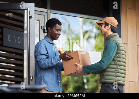 Side view portrait of black young man accepting grocery delivery outdoors and smiling Stock Photo