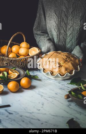 Orange Pie with decorative pastry top on a marble kitchen surface held by a woman Stock Photo