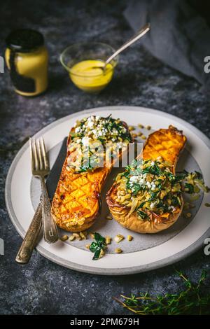 Mustard Glazed Butternut Squash Halves Stuffed with Farro and Kale on Plate with glaze in bowl, side angle Stock Photo