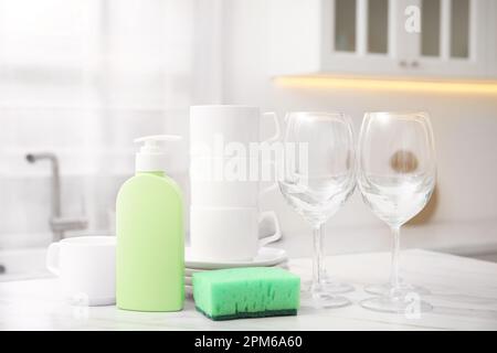 Clean glasses, cups and cleaning product on table in stylish kitchen Stock Photo