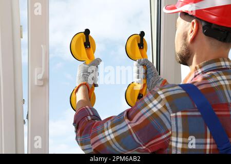 Worker using suction lifters during plastic window installation indoors Stock Photo