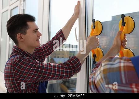 Workers using suction lifters during plastic window installation indoors Stock Photo
