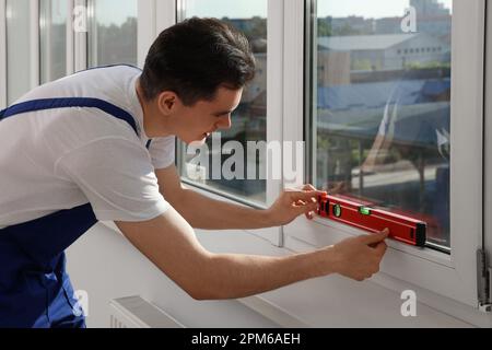 Worker using bubble level after plastic window installation indoors Stock Photo