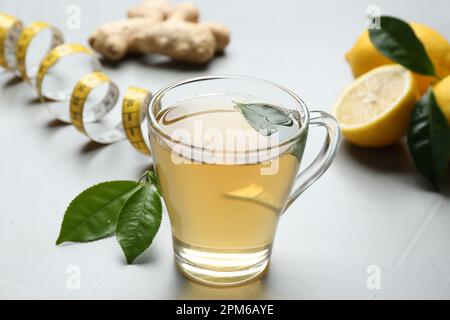 Herbal diet tea, lemon, ginger and measuring tape on light table Stock Photo