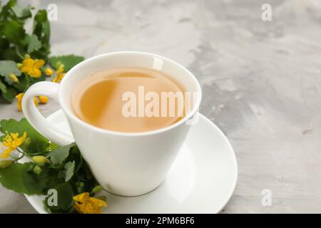 Cup of aromatic celandine tea and flowers on grey table, closeup Stock Photo