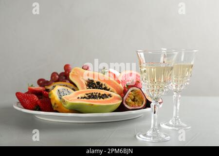 Delicious exotic fruits and glasses of wine on light grey table Stock Photo