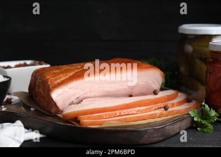 Delicious smoked bacon with spices and parsley on black table, closeup Stock Photo