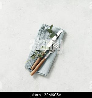 Table setting with linen napkin, fork, knife and eucalyptus on grey background square composition Stock Photo