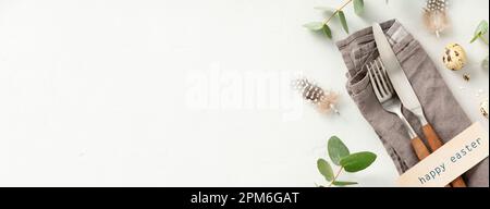 Easter table decorations. Stylish Easter brunch table setting with vintage cutlery, easter eggs and spring branches on light grey background top view Stock Photo