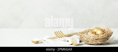 Easter table decorations with cutlery, spring flowers and golden eggs on light grey background copy space Stock Photo