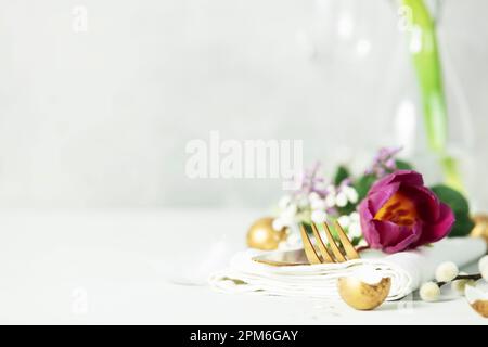 Easter table decorations with cutlery, spring flowers and golden eggs on light grey background copy space Stock Photo