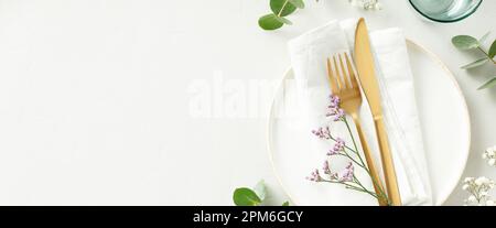 Gold Cutlery with eucalyptus branches on white plate with napkin over light grey Background. Minimalistic design. Copy Space Stock Photo