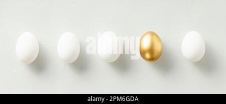 White chicken eggs with one golden egg flat lay top view banner. standing out from the crowd Stock Photo