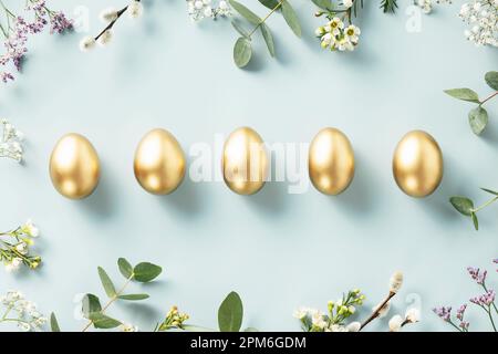 Easter decorations. Happy Easter concept with golden easter eggs, feathers and spring flowers on blue background. Flat lay Stock Photo