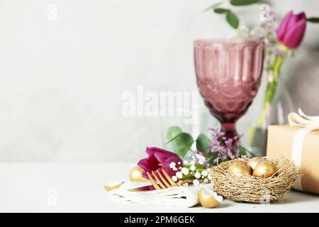 Easter table decorations with cutlery, spring flowers and golden eggs on light grey background copy space Stock Photo