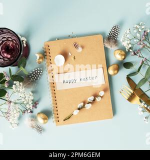 Easter table decorations. Happy Easter concept with white plate, golden easter eggs, feathers and spring flowers on blue background. Flat lay top view Stock Photo