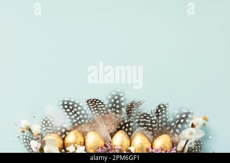 Raw of golden quail eggs and quail feathers on blue background. Beautiful modern minimalistic Easter composition. Copy space, top view, flat lay Stock Photo