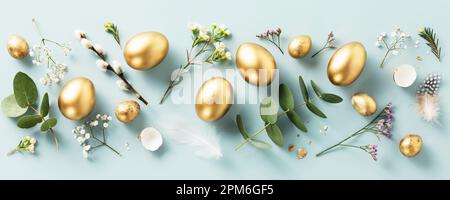 Easter composition of golden quail eggs, feathers and spring flowers over pastel blue background. Springtime holidays concept. Minimalist modern Easte Stock Photo
