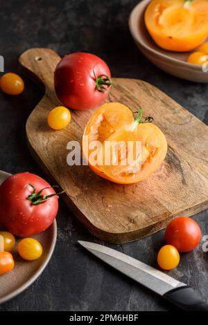 Half a tomato on a cutting board. There are various yellow and red tomatoes nearby. Stock Photo